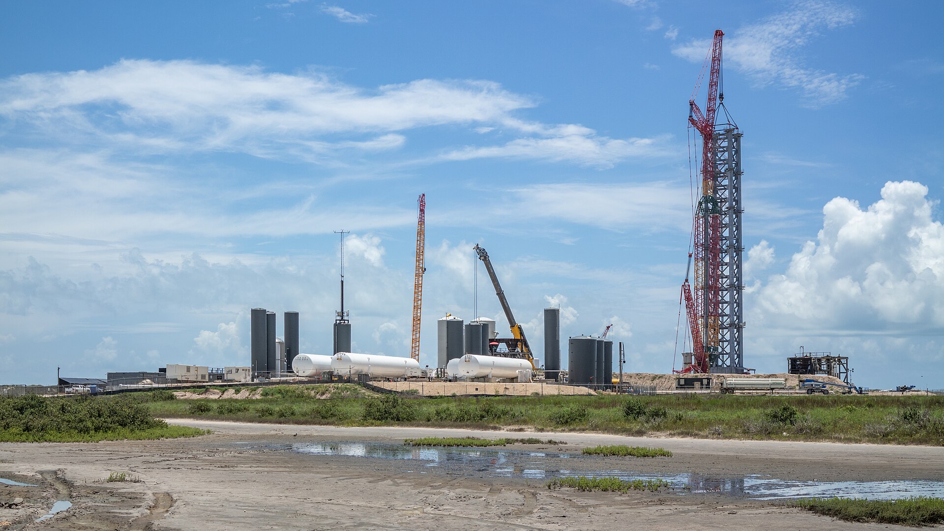SpaceX's Starbase launch site in Boca Chica, Texas: storage tanks and a tall launch tower under construction beside coastal wetlands.